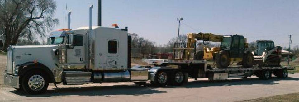 Photo of a diesel tractor with construction equipment on the flatbed.